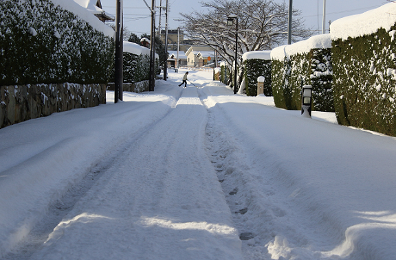 積雪した道路を雪カキをして横切る人